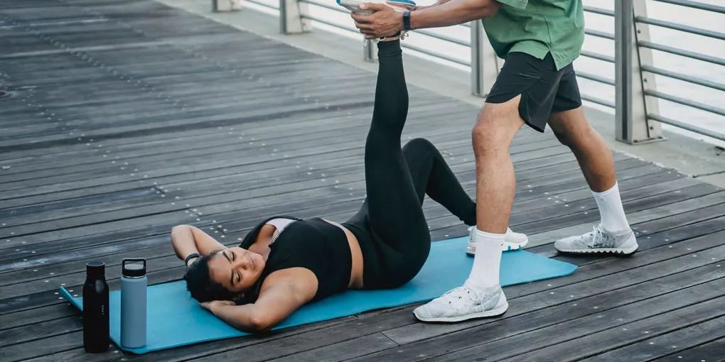 Pessoa alongando a perna sentada sobre um tapete de exercícios