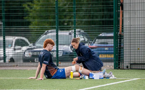 Fisioterapeuta esportiva atendendo atleta lesionado à beira do campo