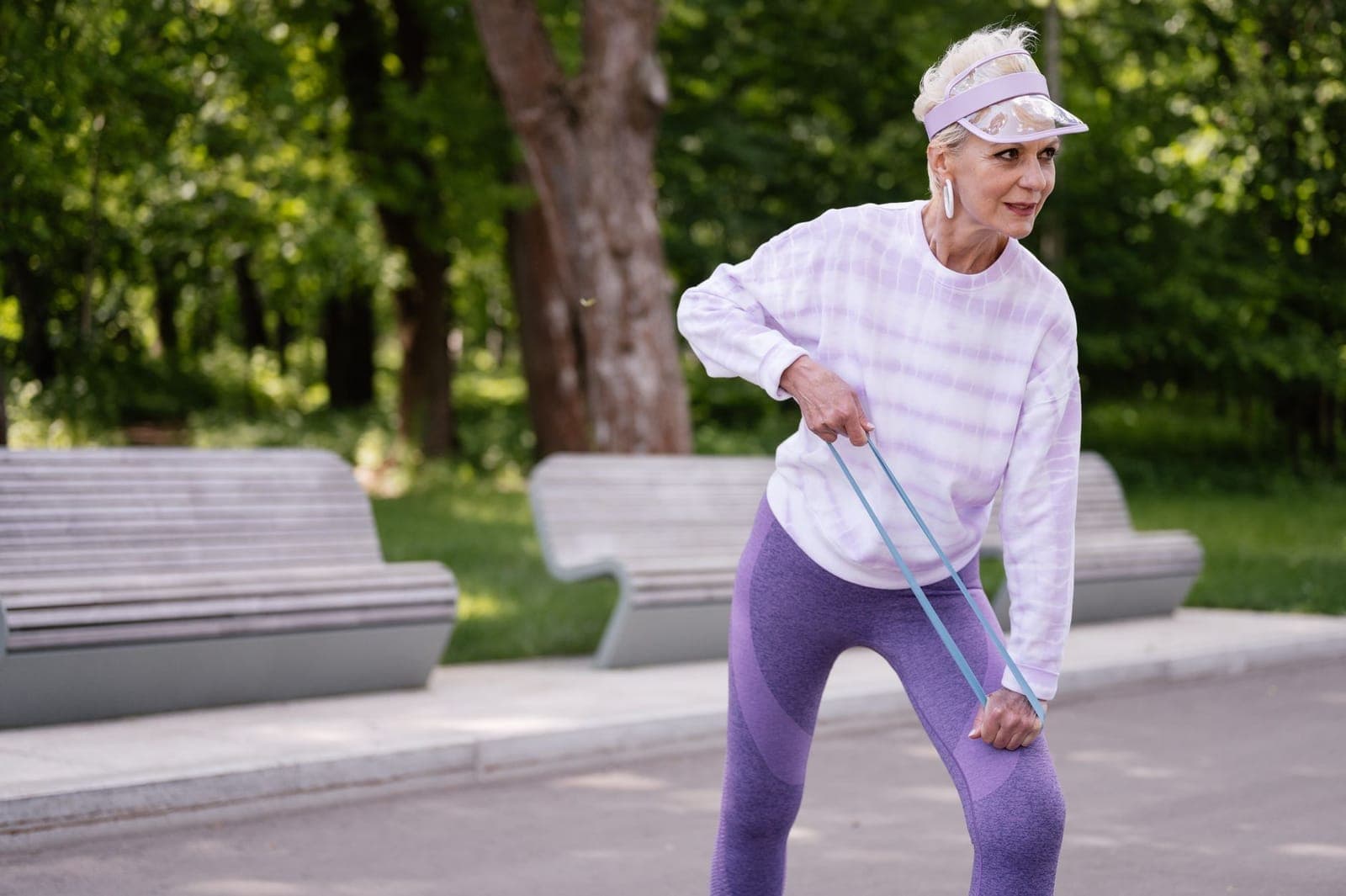 Mulher mais velha ao ar livre realizando exercício de fortalecimento com faixa elástica