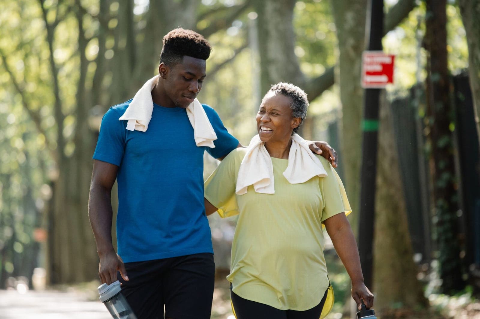 Jovem e mulher mais velha caminhando juntos em um parque arborizado depois de se exercitar