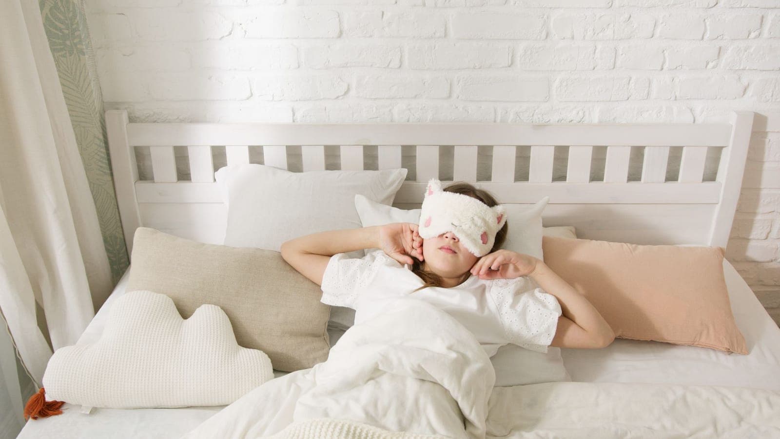 Mulher deitada na cama com máscara de dormir, tentando descansar durante o dia